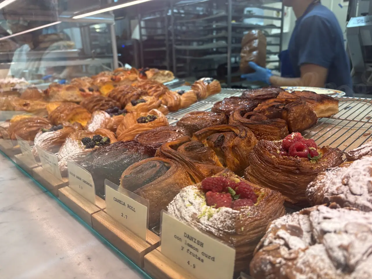 Display case of assorted pastries including cinnamon rolls and berry danishes with price cards