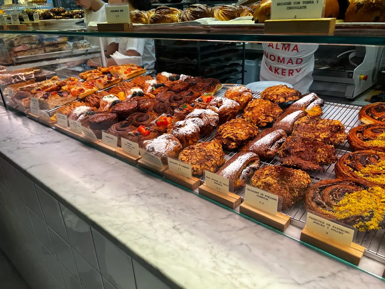 Long display case of pastries including almond croissants, cinnamon rolls and fruit danishes with price cards