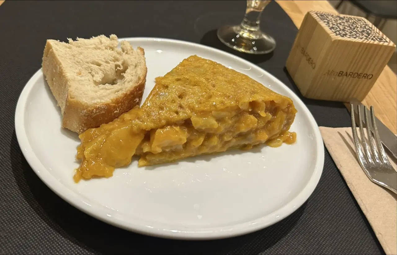Slice of runny Spanish tortilla with a piece of bread on a white plate