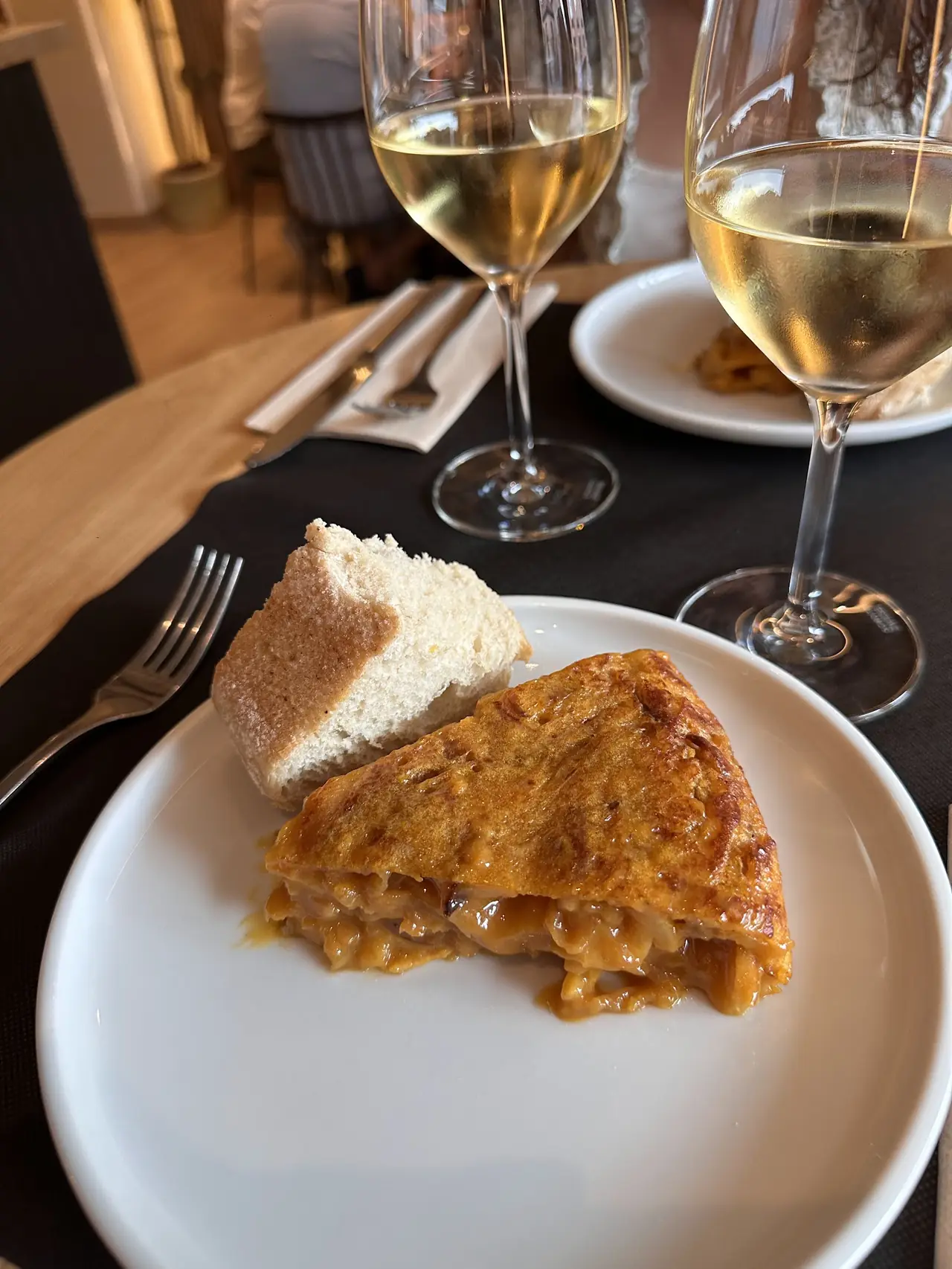 Slice of Spanish tortilla with bread and glasses of white wine on the table