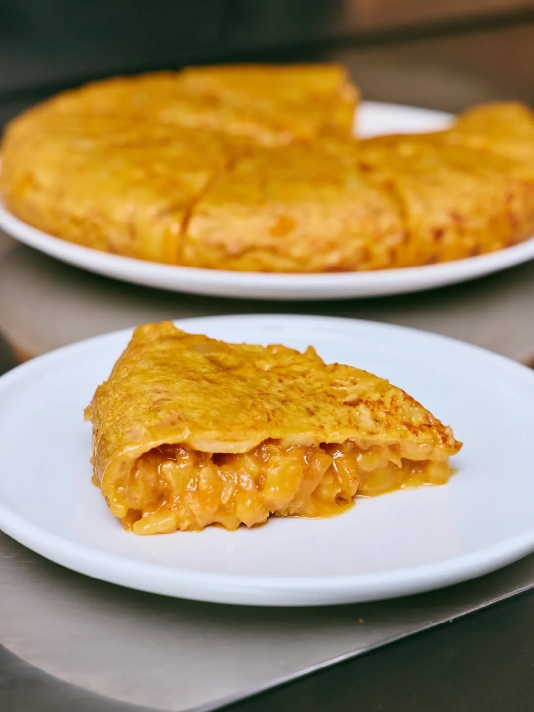 A whole potato omelette and a cut slice on white plates