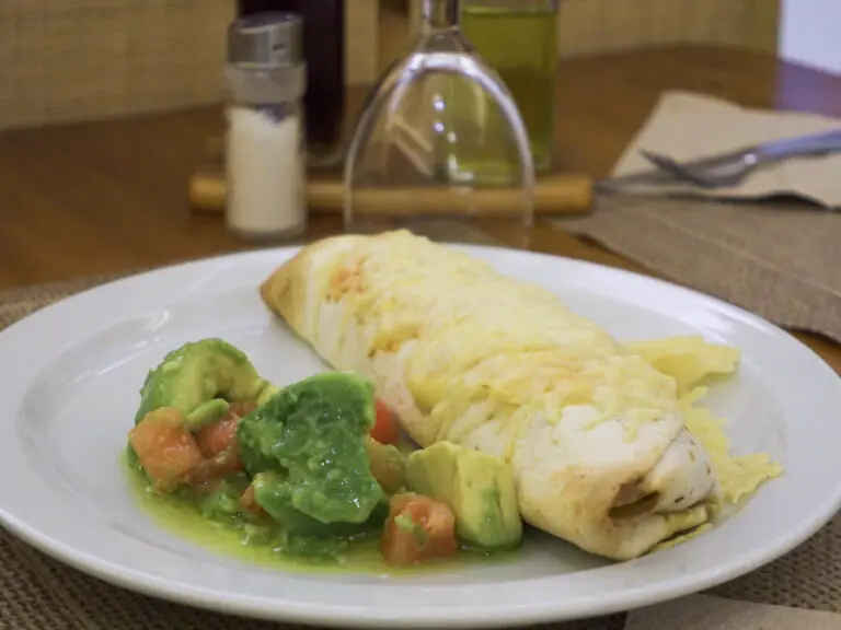 Cheese-topped burrito on a white plate with a side of chunky avocado and tomato salsa, at Amaltea