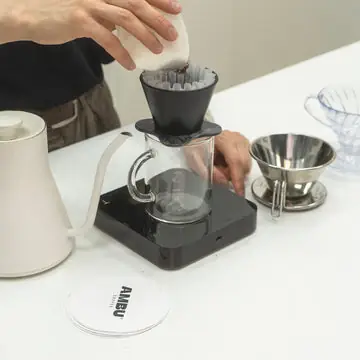 Barista brewing pour-over coffee with a gooseneck kettle over a glass carafe