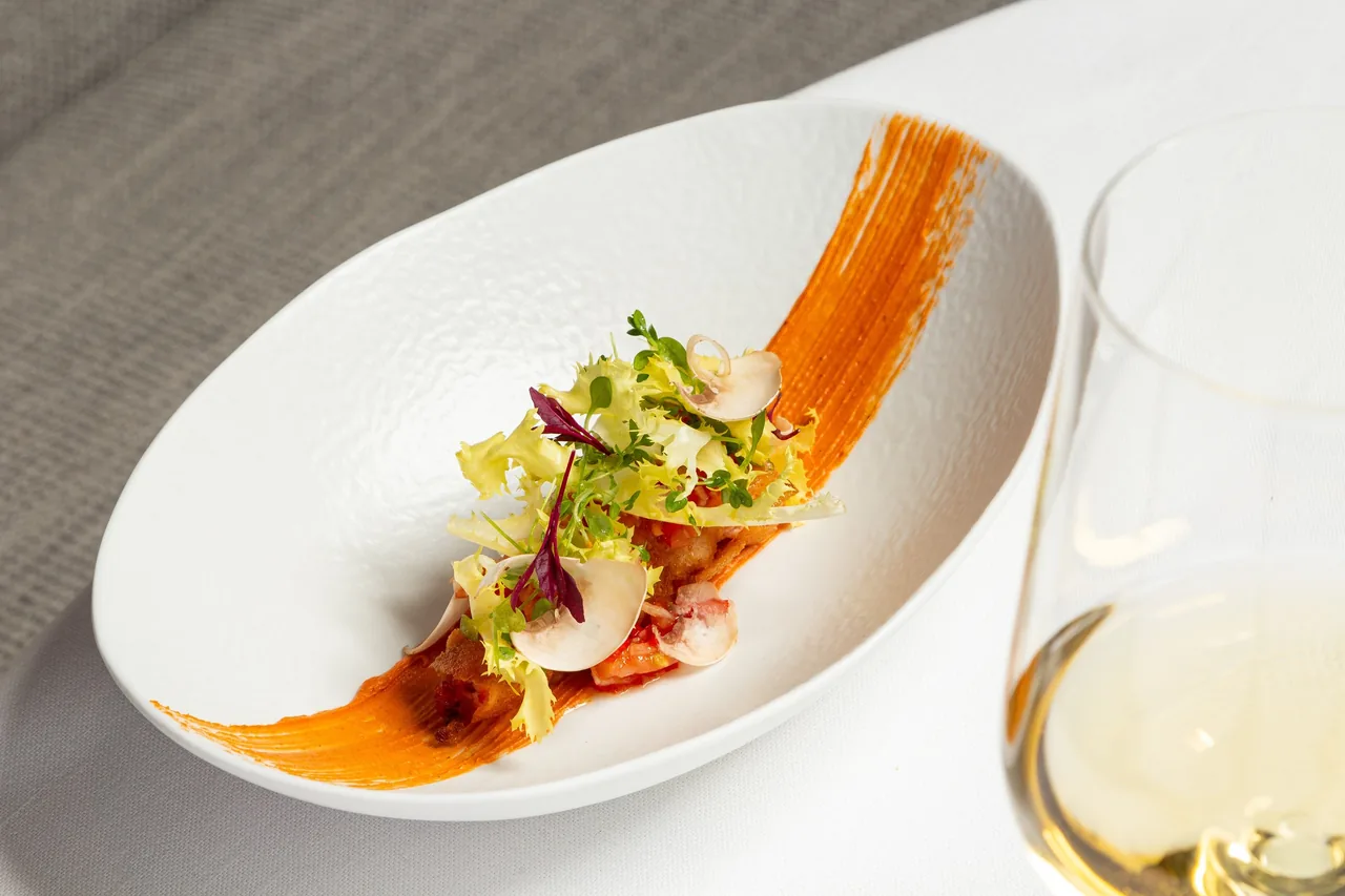 A white bowl of colourful salad with a sweep of orange sauce