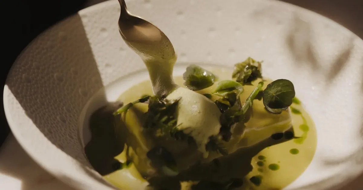 A white bowl of green sauce with small green garnishes