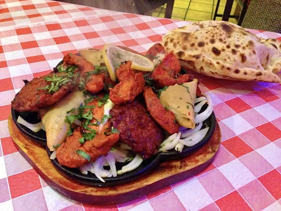 Grilled meat pieces on a sizzling platter over onions, with naan bread
