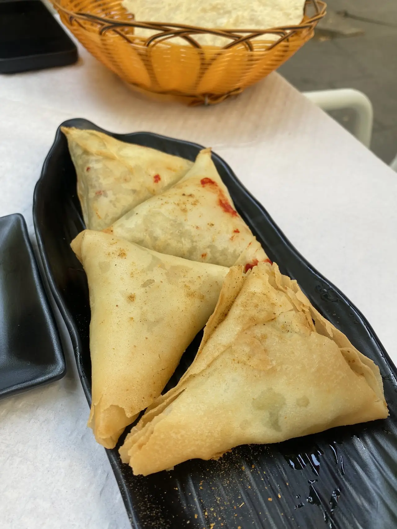 Two triangular fried samosas on a dark plate.