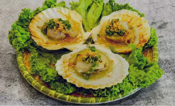 Three grilled scallops on the half-shell topped with garlic and scallion, plated over lettuce