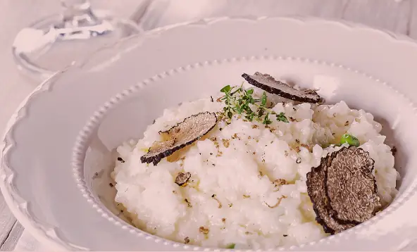 Creamy risotto in a white bowl topped with shaved black truffle and fresh herbs