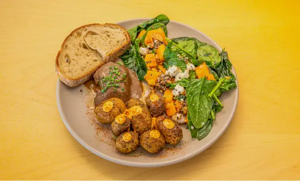Plate of meatballs in sauce with a slice of sourdough and a spinach, squash and blue-cheese salad