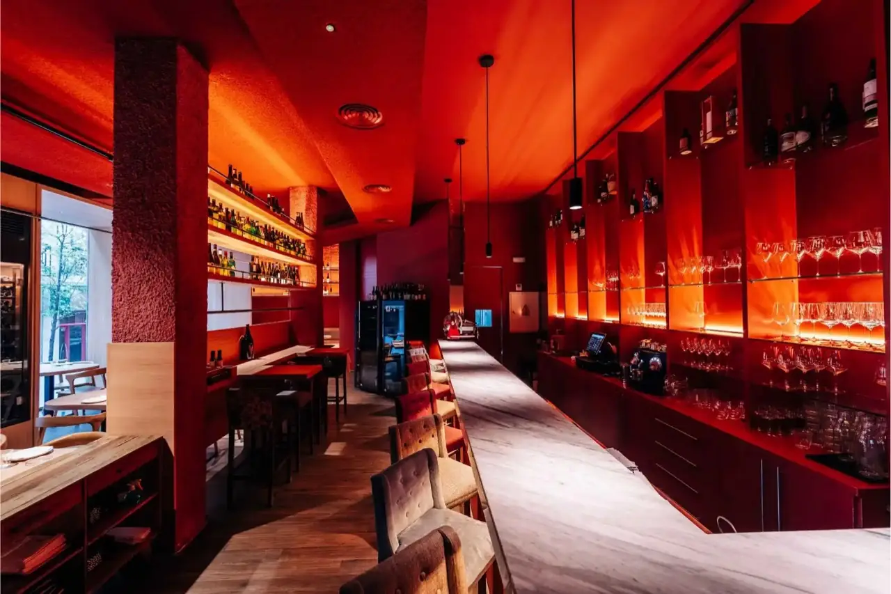 Red-lit wine bar interior with a long marble counter, glassware shelves and wine bottles along the walls