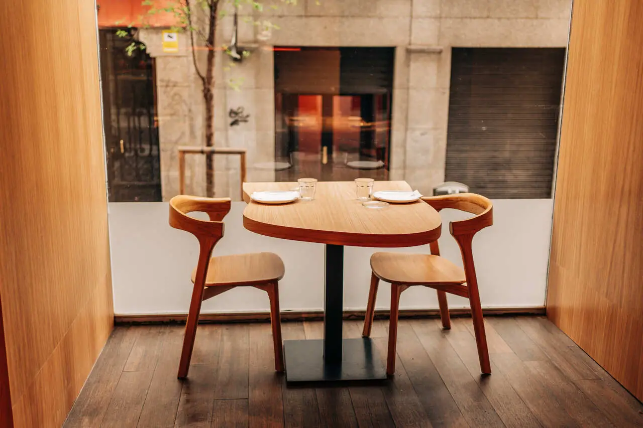 Set wooden dining table for two with chairs beside a window looking onto the street