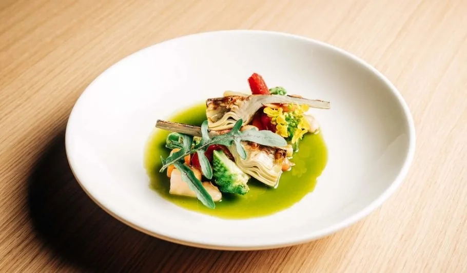A white plate of fish and vegetables in a bright green sauce