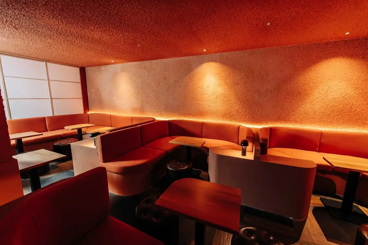 A red banquette seating area with tables in a warmly lit bar