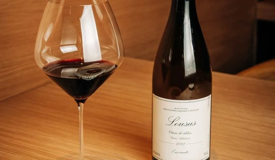 A glass of red wine beside a bottle on a light wooden table