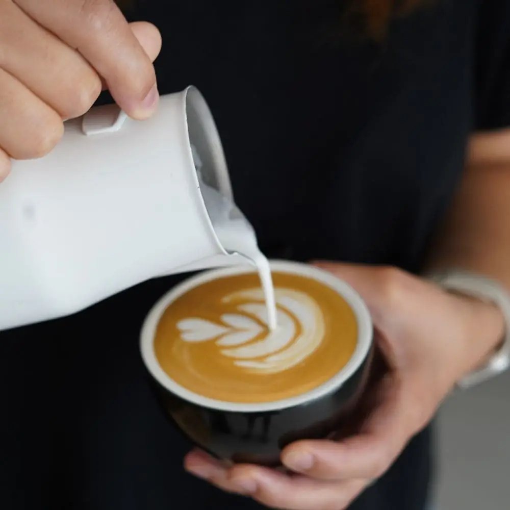 Barista pouring steamed milk into a black cup of espresso, forming latte art, Animal Coffee Roasters