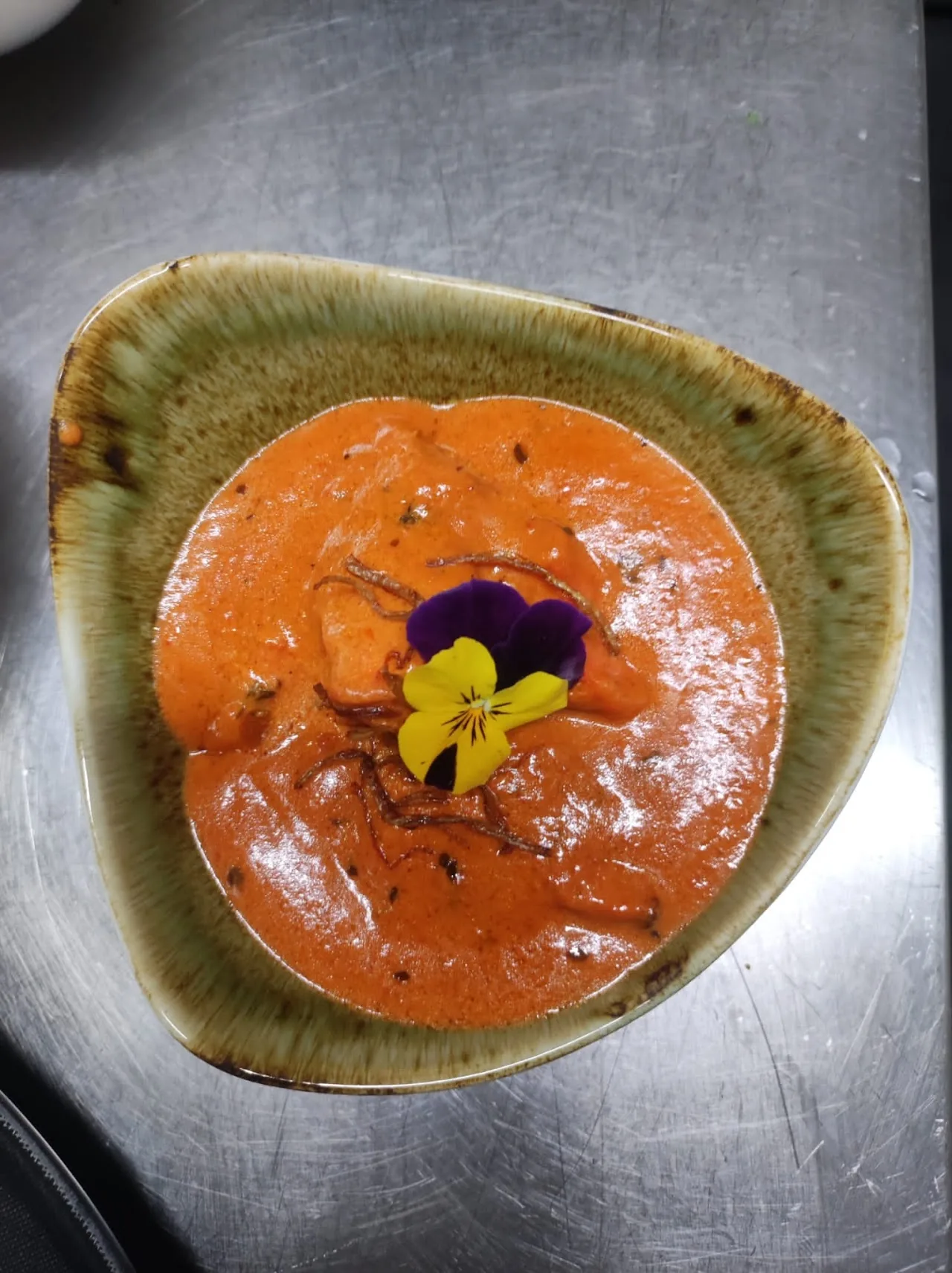 A bowl of orange curry garnished with a purple flower