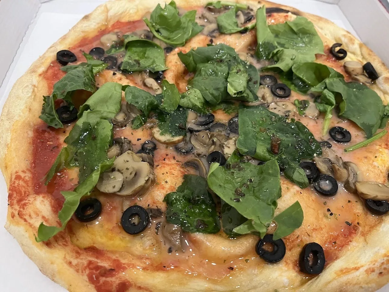 A pizza topped with spinach leaves, mushrooms and black olives