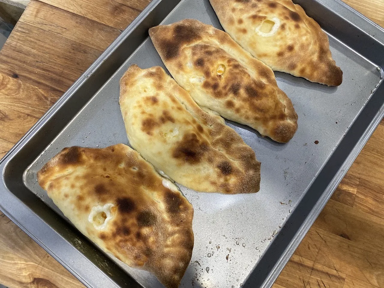 Three baked calzones on a metal tray