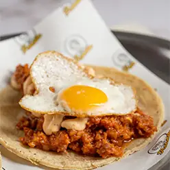 Tostada topped with spiced meat and a fried egg on branded paper