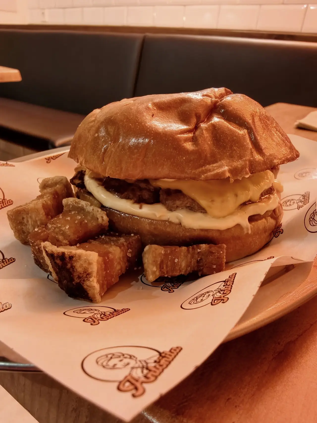 A cheeseburger with crisp pork crackling pieces on a tray lined with branded paper