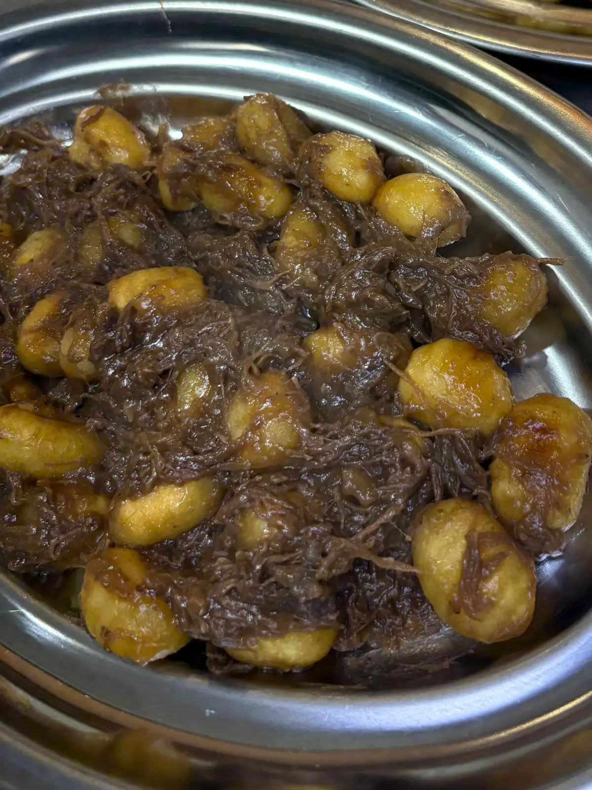 A metal platter of gnocchi with a dark braised-meat sauce