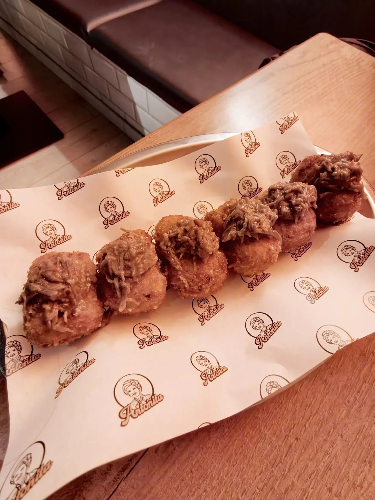 A row of crumbed croquettes on branded paper on a metal tray