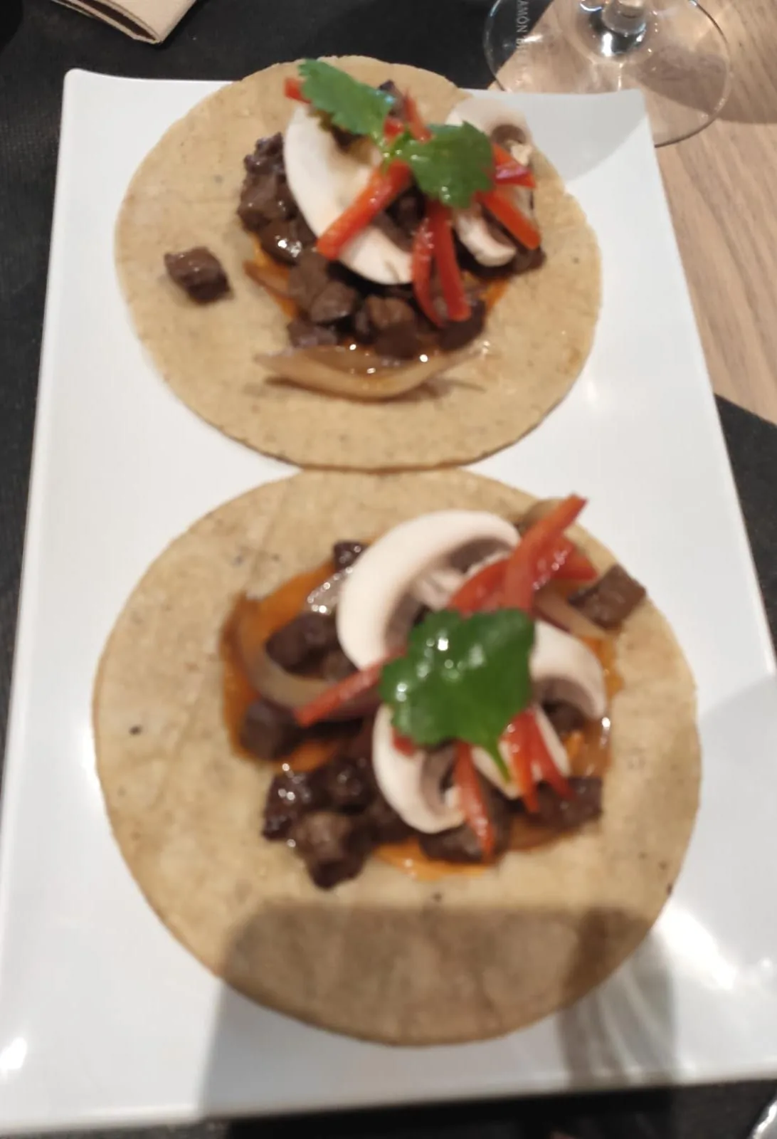 Two soft tacos topped with grilled meat, red pepper strips, and cilantro