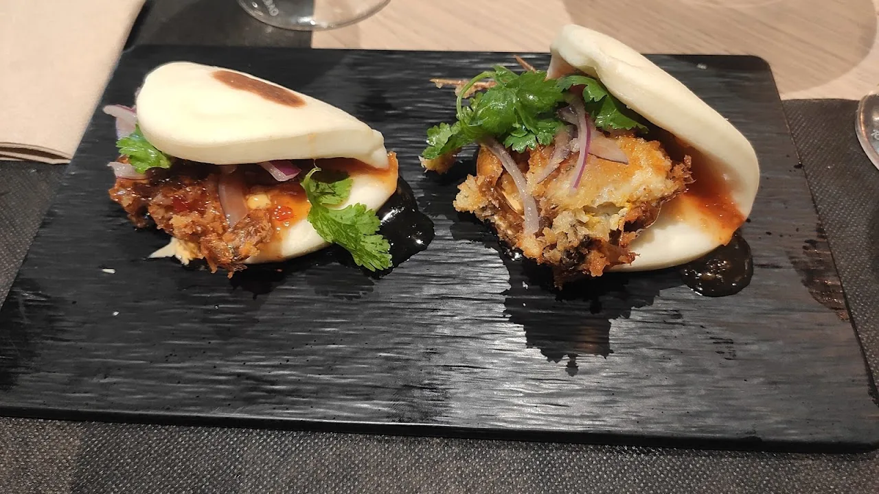 Two crispy croquette-topped bao-style buns with a swirl of orange sauce