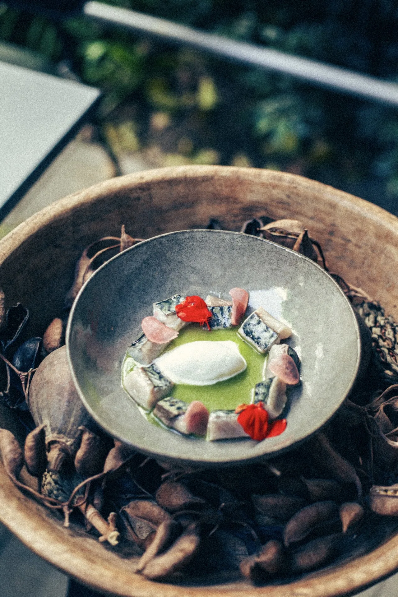 A small dish of green sauce with radish garnish, plated in a bowl of dried leaves