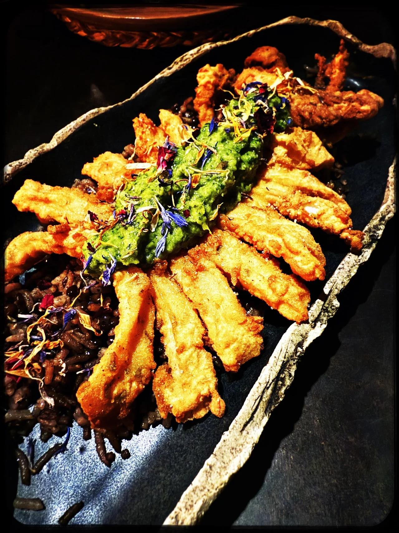 A fan of golden fried food pieces drizzled with green sauce and edible flowers