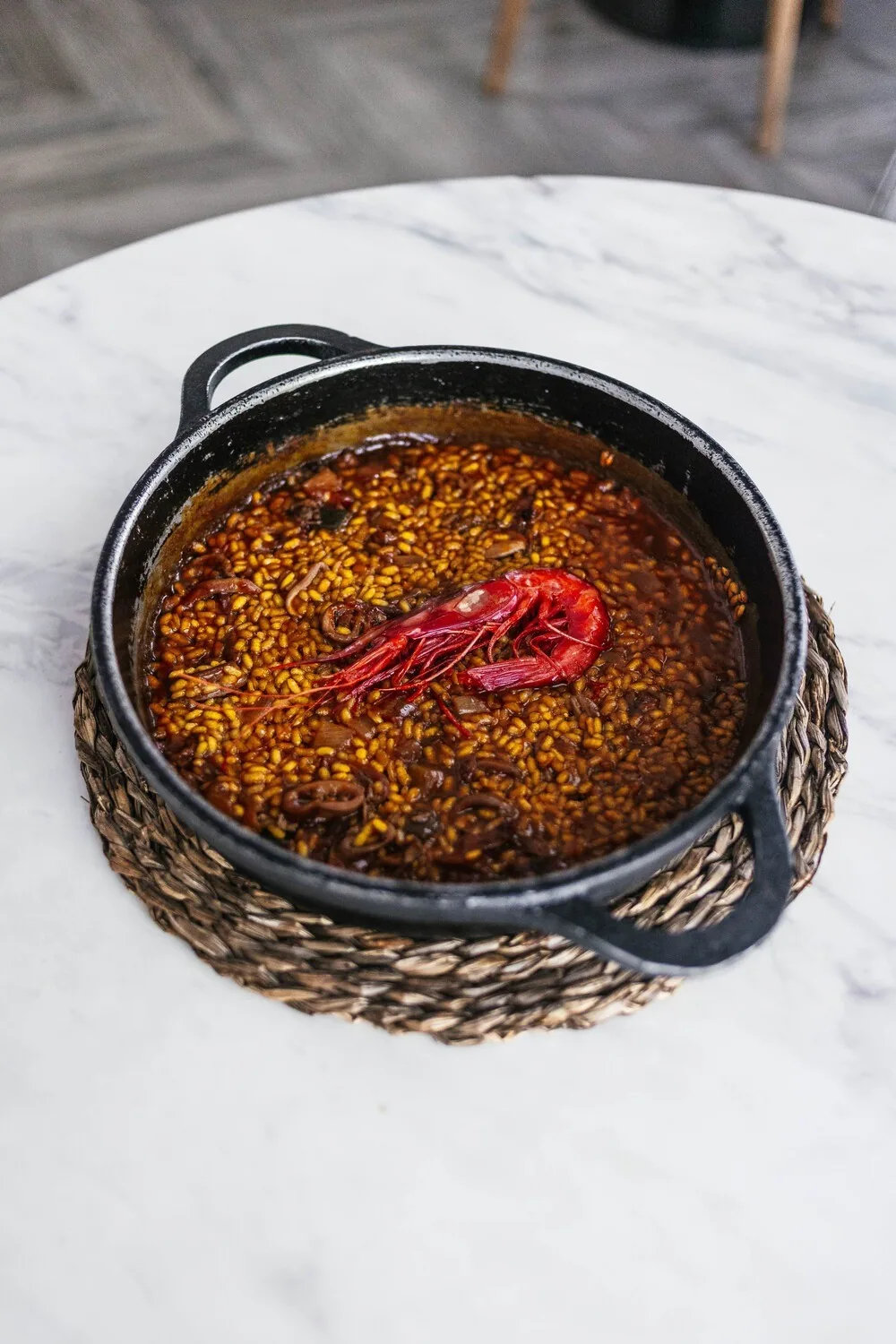 A small black pan of golden rice topped with a red prawn on a marble table