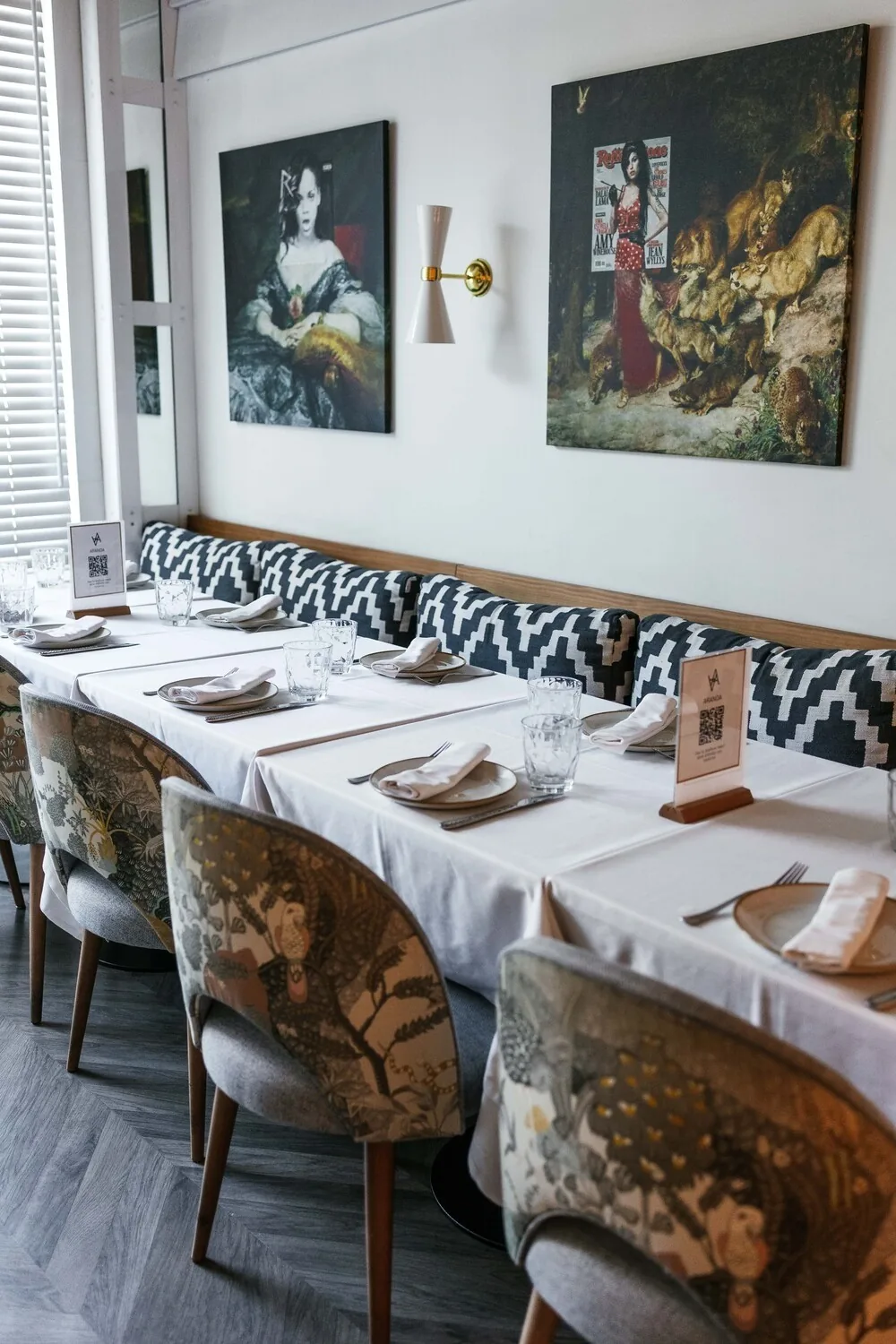 A dining room with set tables, cushioned benches and framed paintings