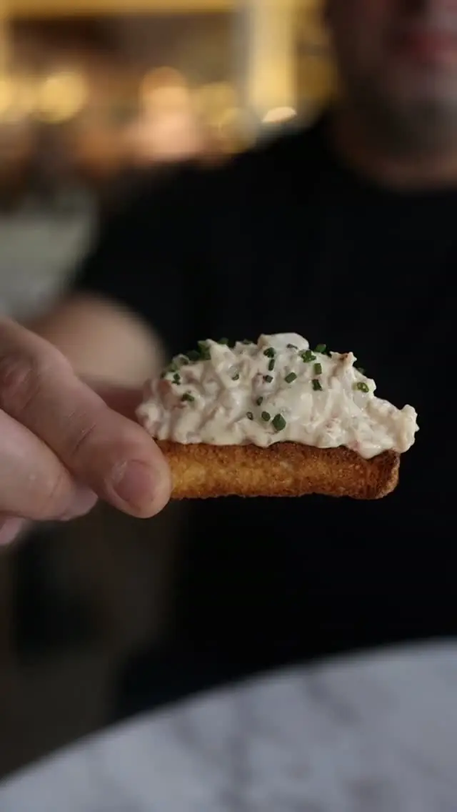 Toast topped with creamy seafood salad and chives held in a hand