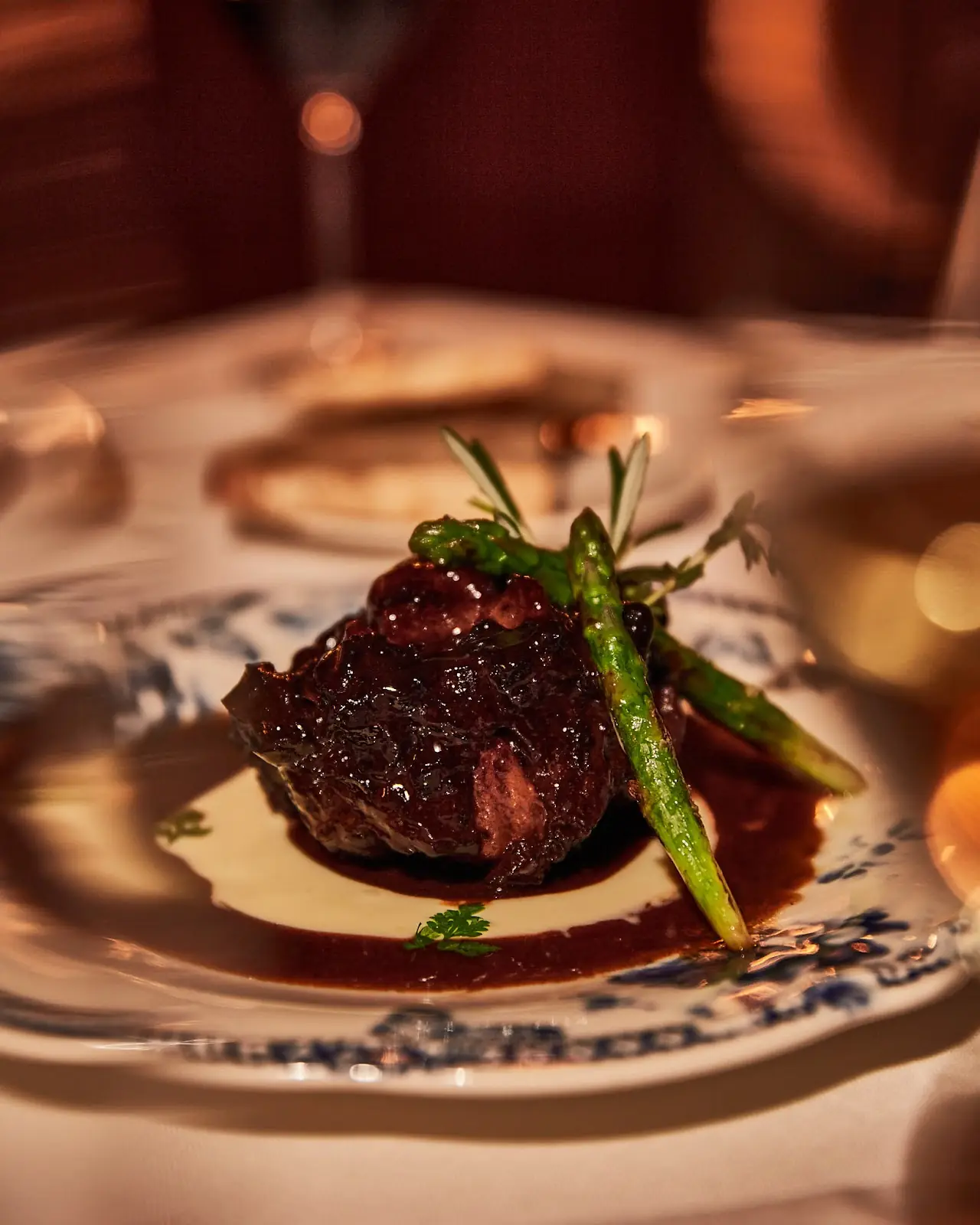 A plated steak with a charred green vegetable on a patterned dish.