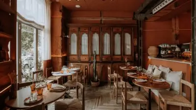 Warm terracotta-toned dining room with wooden furniture, rush-seated chairs, a tall antique glazed cabinet and set tables with amber glassware