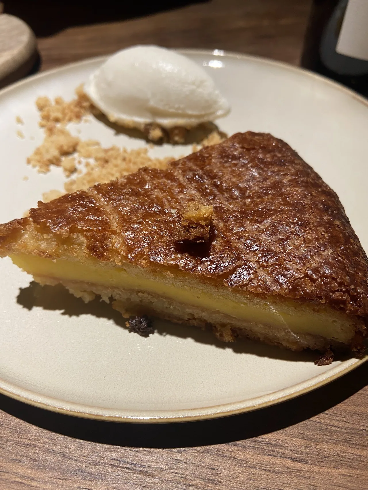 A slice of golden tart with a scoop of ice cream on a round plate