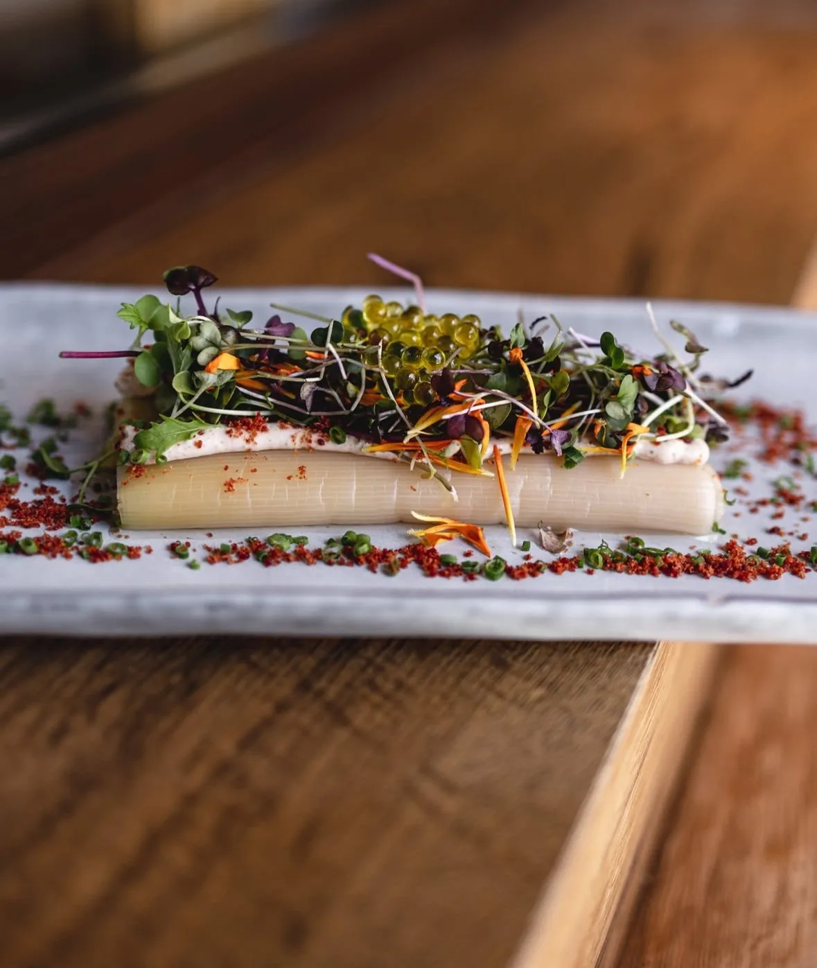 A long white plate topped with a pale slice, herbs and microgreens on a wooden table