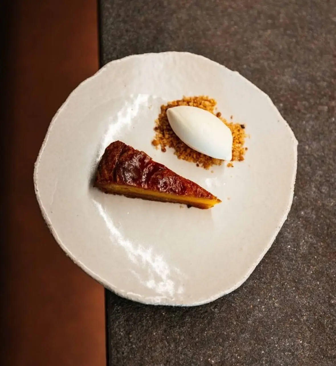 Slice of caramelized Basque cake with a quenelle of ice cream and crumble on a white plate