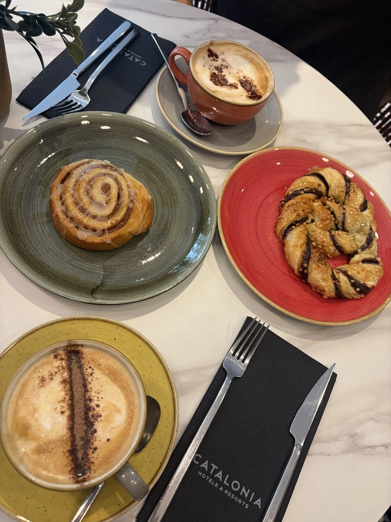 A cinnamon roll, a pastry and a latte arranged on colorful plates