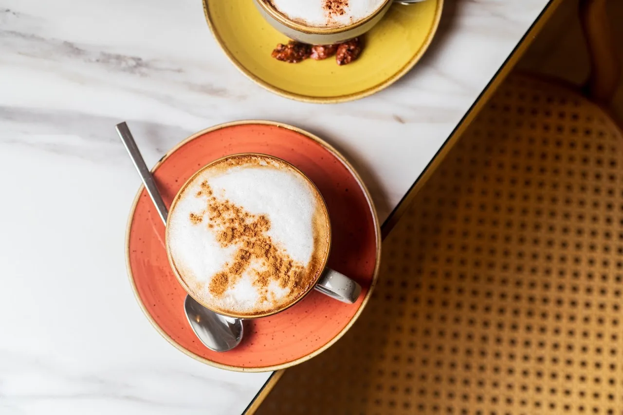 A cappuccino dusted with cinnamon on a yellow saucer, overhead view
