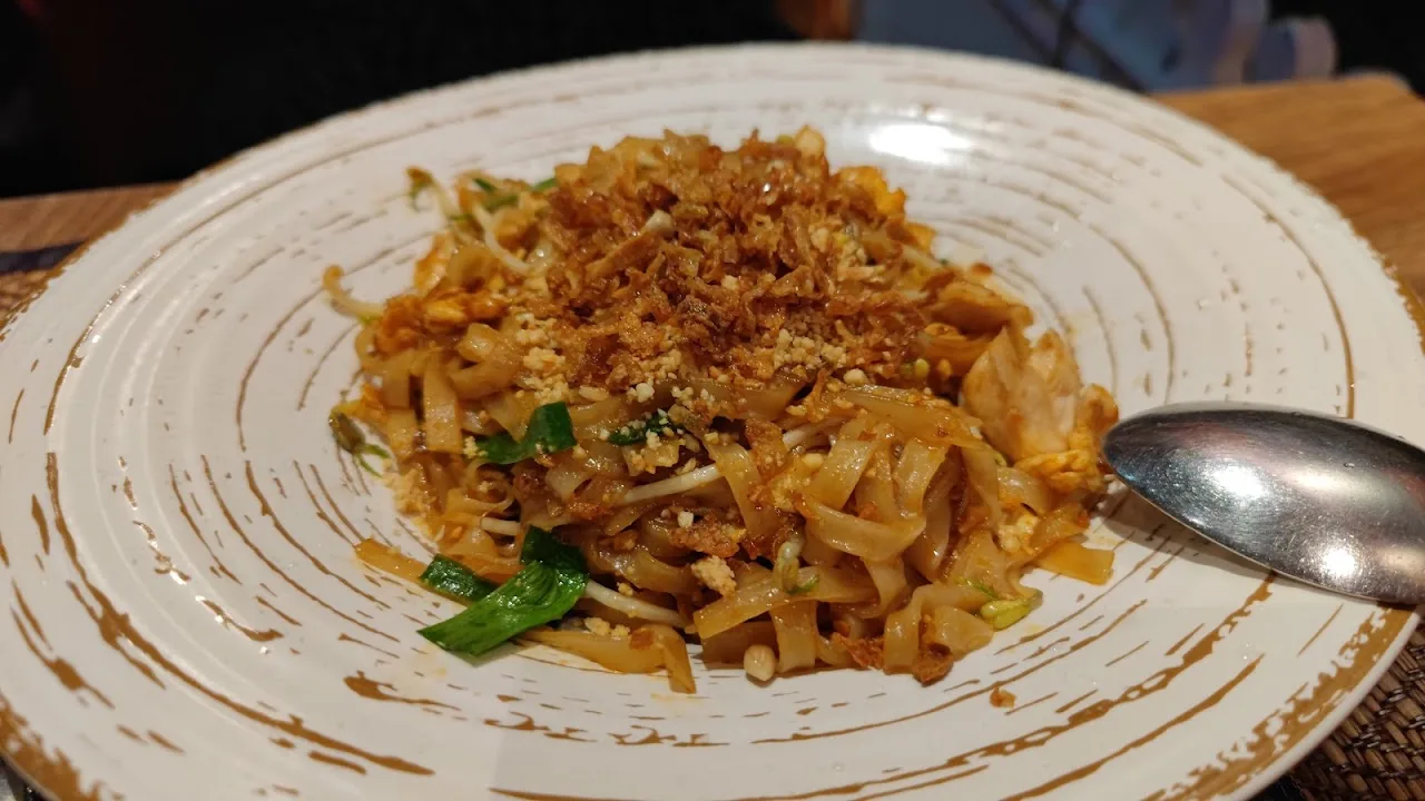 A plate of stir-fried rice noodles with herbs and a spoon