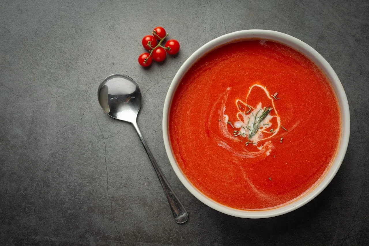 A bowl of red tomato soup garnished with a spoon and cherry tomatoes