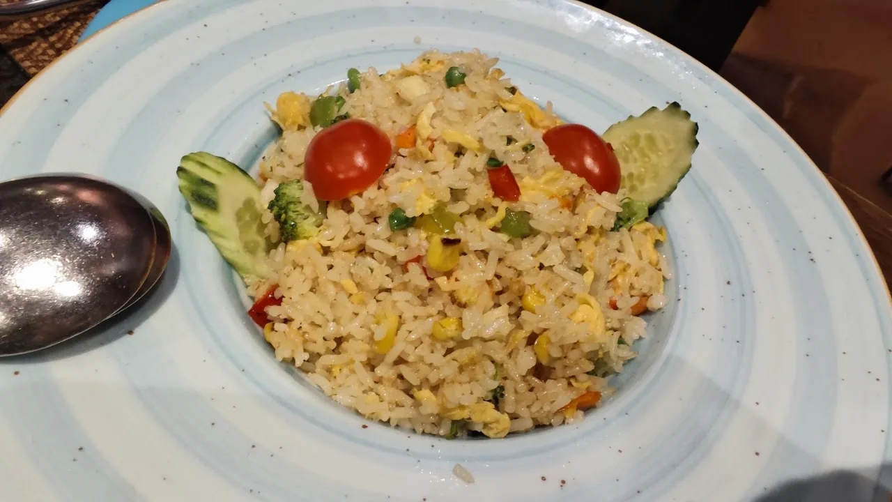 A plate of fried rice with tomato and cucumber garnish
