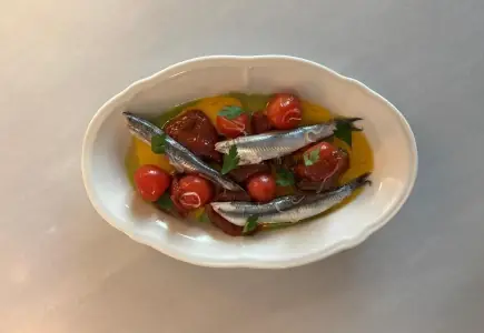 Marinated anchovies with cherry tomatoes and fresh herbs in olive oil, served in a white oval dish, at Arraval