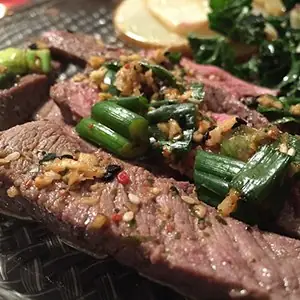 Sliced grilled beef topped with charred scallions and a chopped garlic-herb dressing on a glass plate