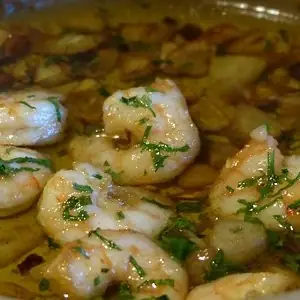 Gambas al ajillo, prawns sizzling in garlic oil with chopped parsley in a pan