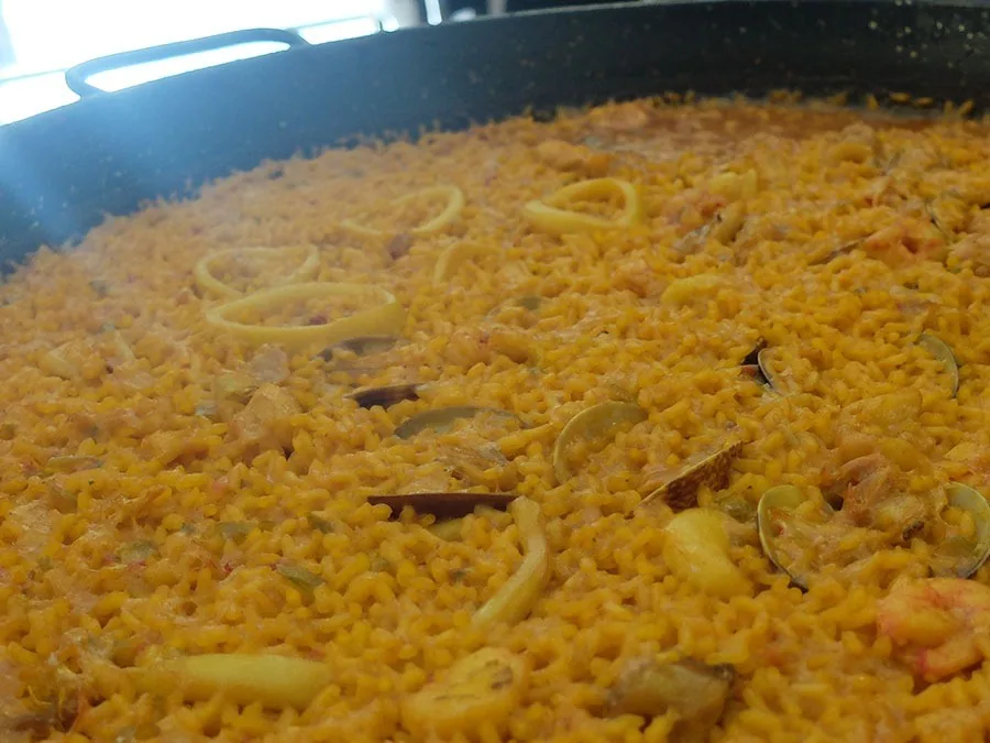 Close view of a large paella pan of yellow rice with squid rings and clams