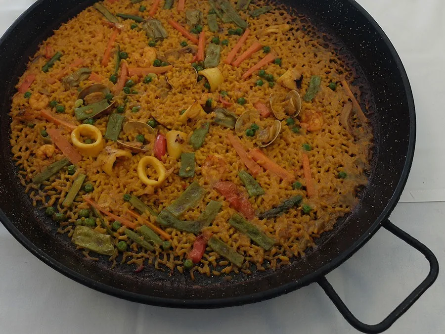 A black paella pan of golden rice and vegetables seen from above