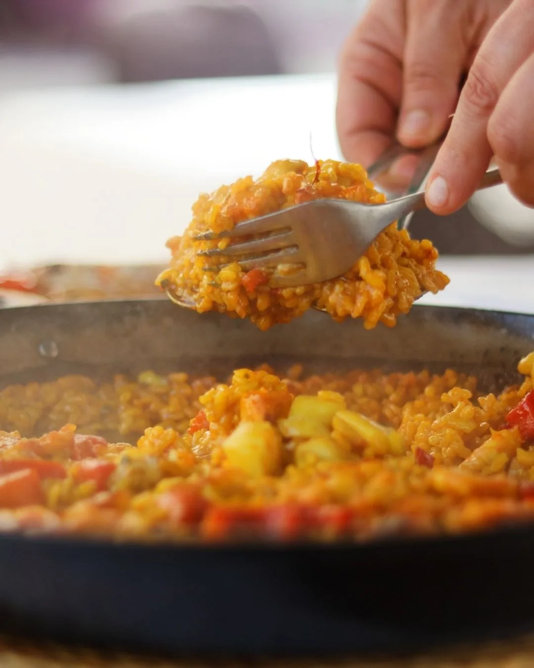 A fork lifting yellow rice from a paella pan